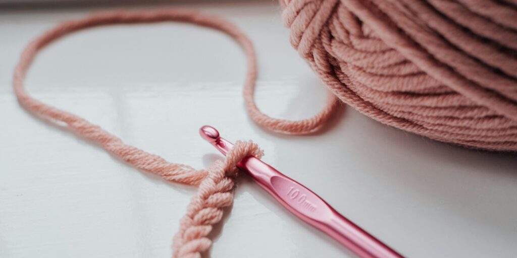 Close-up of pink yarn and crochet hook on a bright indoor windowsill, showcasing a cozy creative hobby.