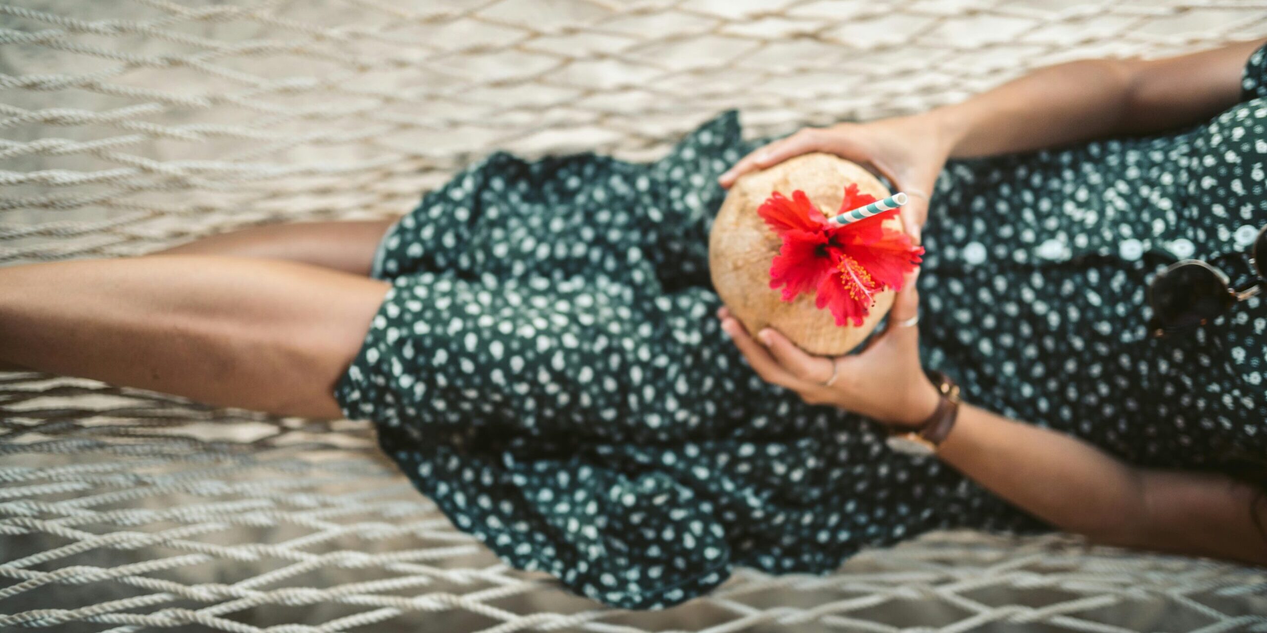 Woman relaxing on a hammock with a tropical coconut drink in a summer setting.