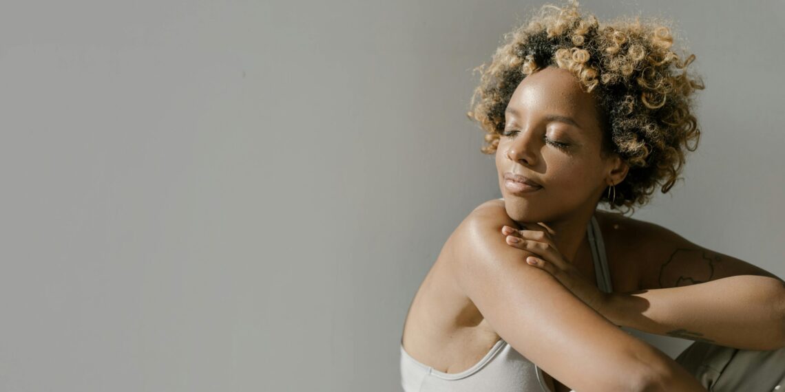 A serene young woman enjoys sunlight indoors, embracing a moment of calm.