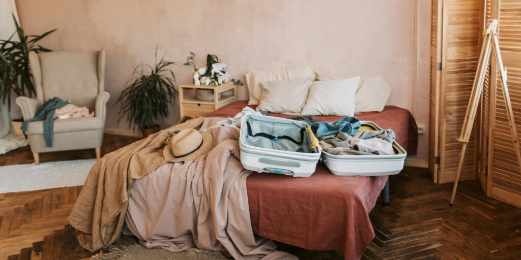 Open suitcase on a bed in a cozy, warmly decorated bedroom, ready for travel, leaving