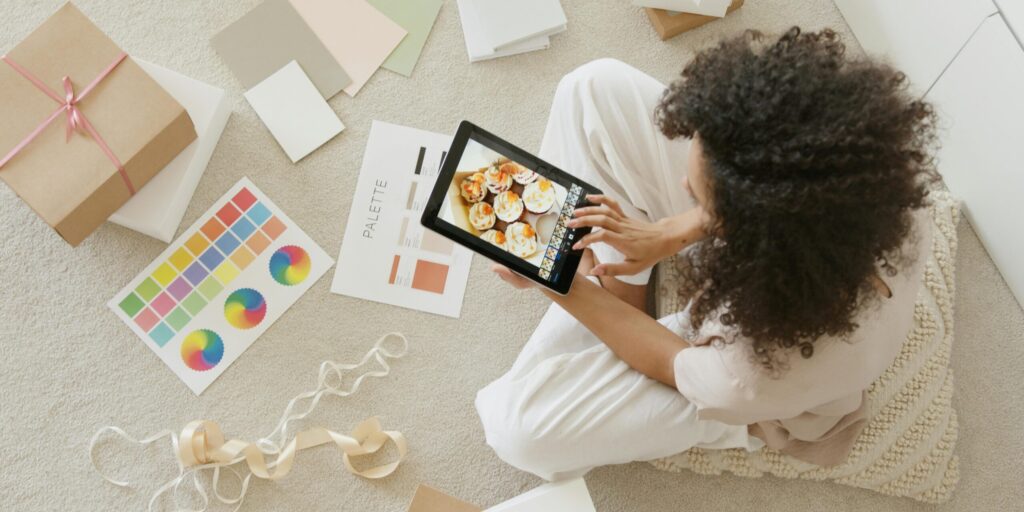 Woman surrounded by art Woman using tablet surrounded by design tools and gift box, showcasing creativity and online work.
