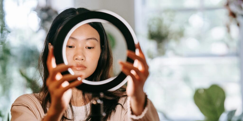 An Asian woman setting up a ring light indoors, focusing on her face and hands.