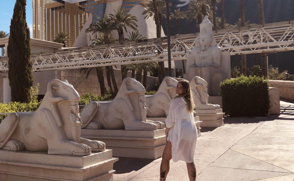 a girl wearing a oversized white shirt posing in front of Luxor hotel in las vegas. statues in background
